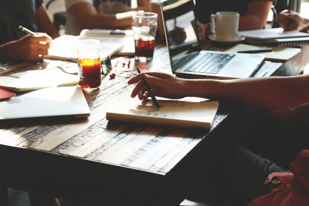 People study around a wooden table with laptops, notebooks, and glasses of iced drinks.