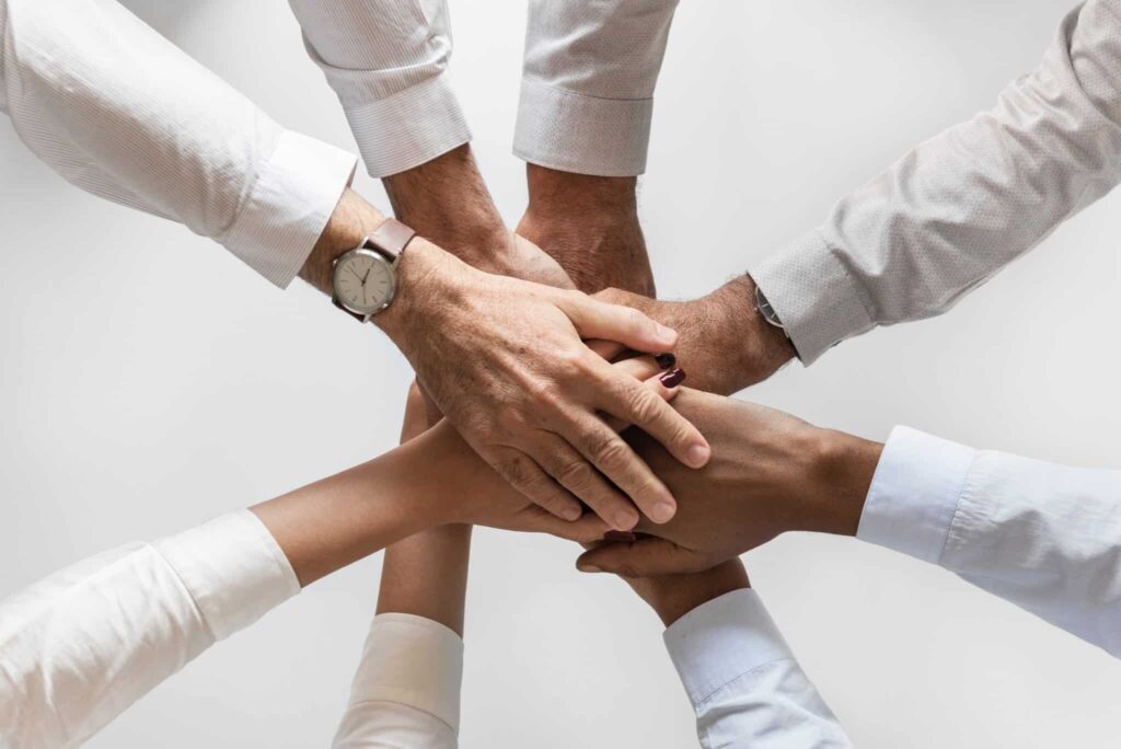 Five hands stacking together in a gesture of teamwork and unity, against a plain white background.