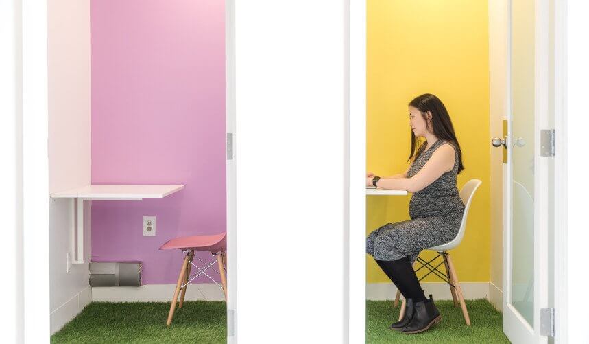 Two side-by-side rooms with pastel walls and grass-like flooring; a woman sits in the yellow room, the pink room is empty.