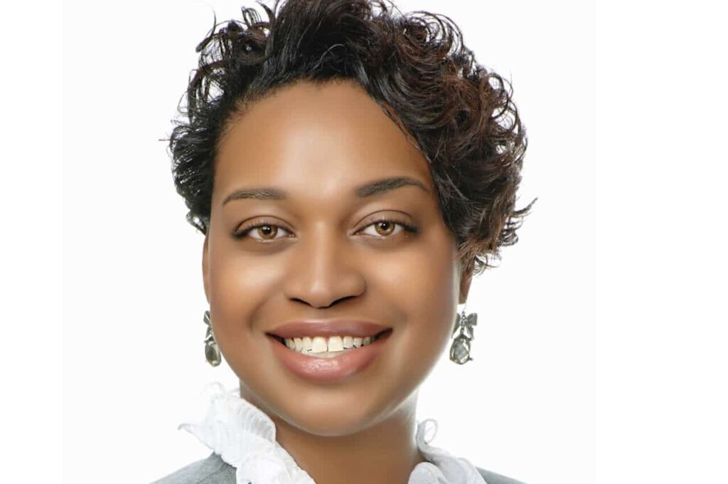Smiling person with short hair, wearing a white shirt and earrings, against a white background.