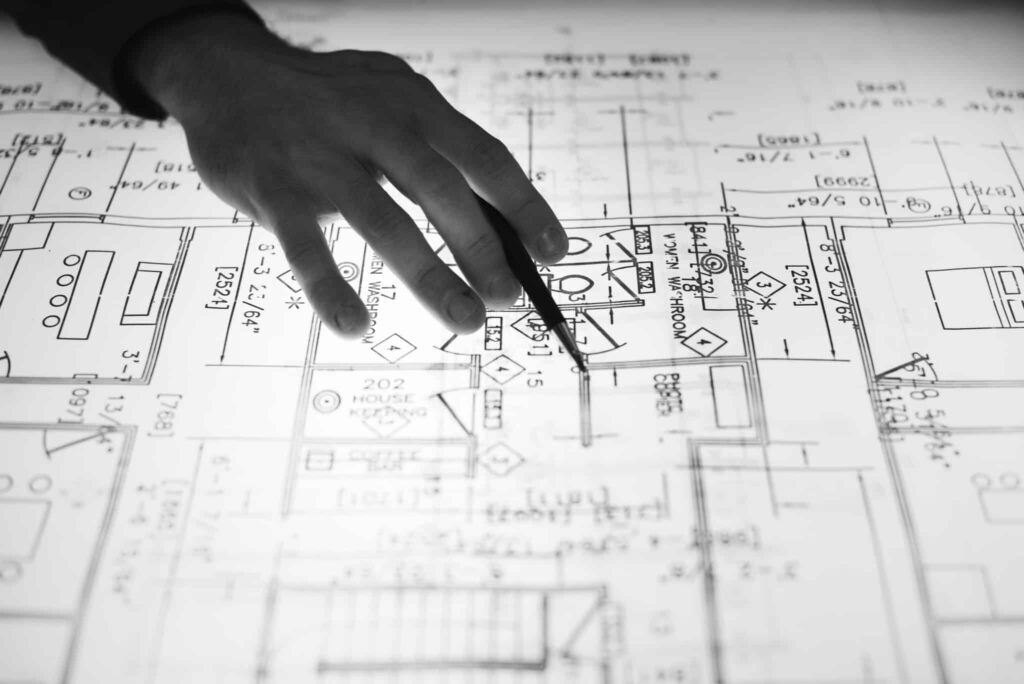 Hand pointing at architectural blueprints on a table.