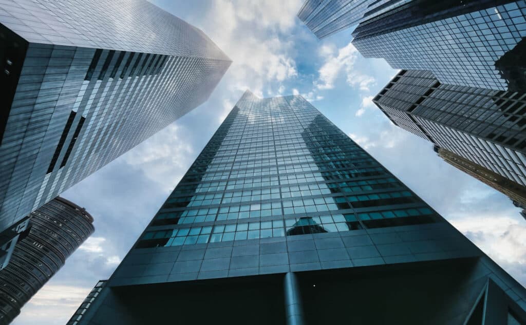 Looking up at modern skyscrapers with glass facades against a cloudy blue sky.