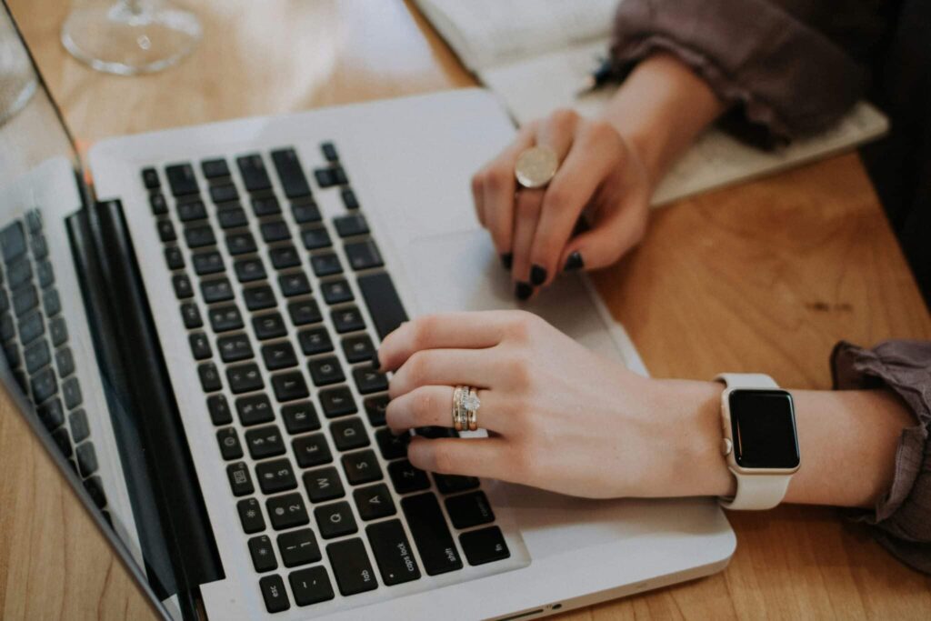 Person wearing a watch and rings using a laptop on a wooden desk.