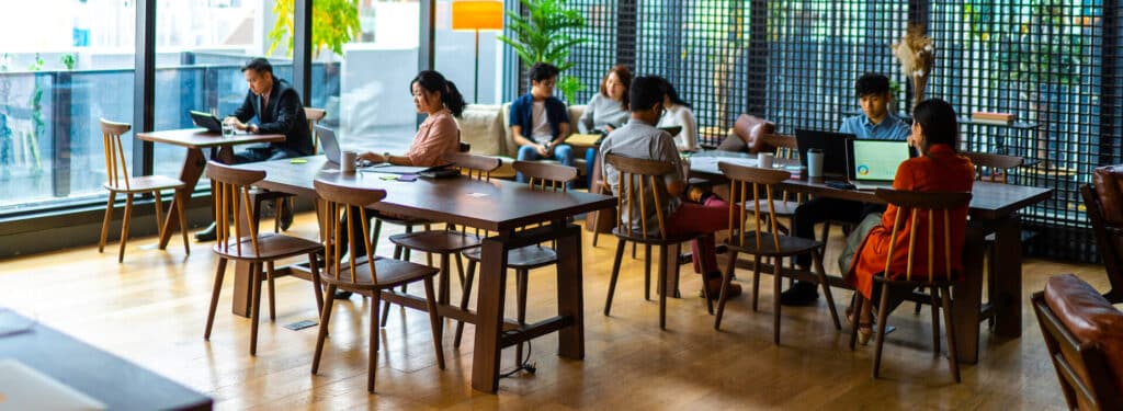 People working on laptops and reading in a modern, open-coffee shop with wooden tables and chairs.