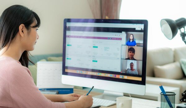 Woman on video call at a desk, working on a large computer monitor with multiple video feeds on screen.