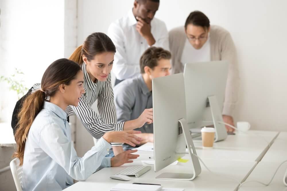 Five people collaborating at a desk with computers in an office setting.
