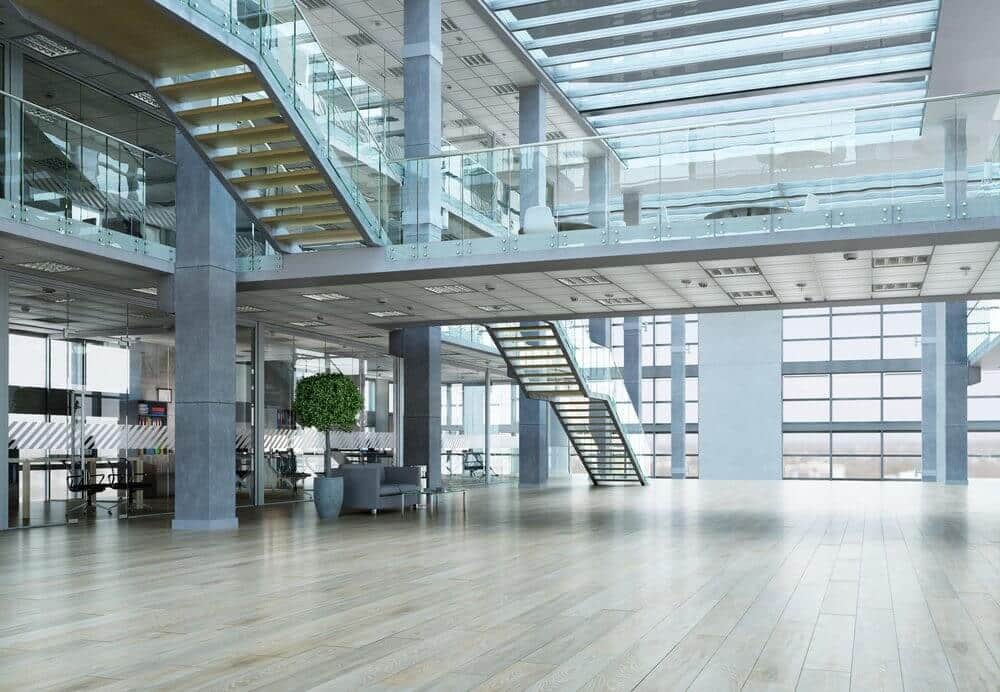 Modern open office space with large windows, glass railings, and wooden floors. Stairs link two floors.