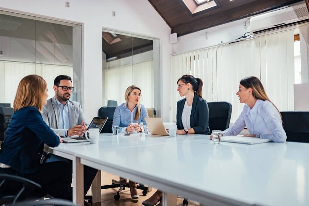 Five people having a meeting around a white table in a modern office setting.