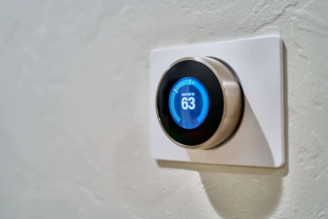 Smart thermostat on a wall displaying temperature set to 63 degrees.
