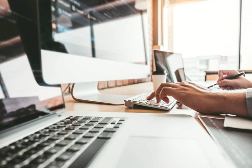 A person typing on a keyboard at a desk with multiple computer monitors and a laptop.