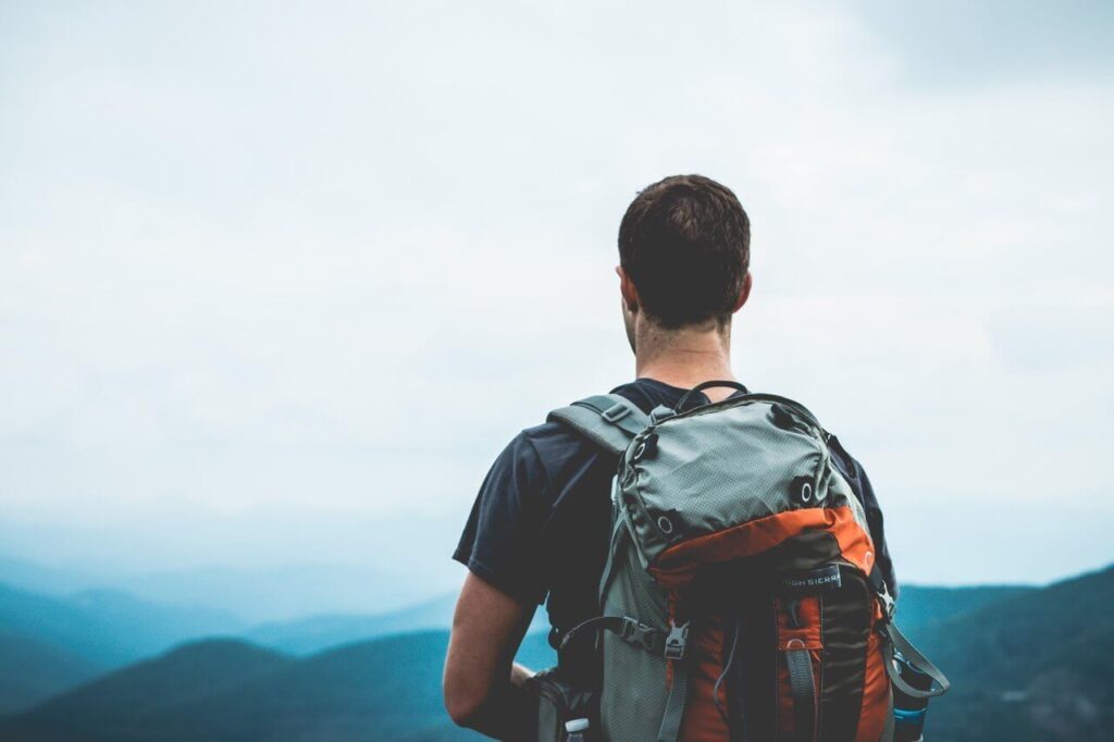 Person with a backpack facing mountains under a cloudy sky.