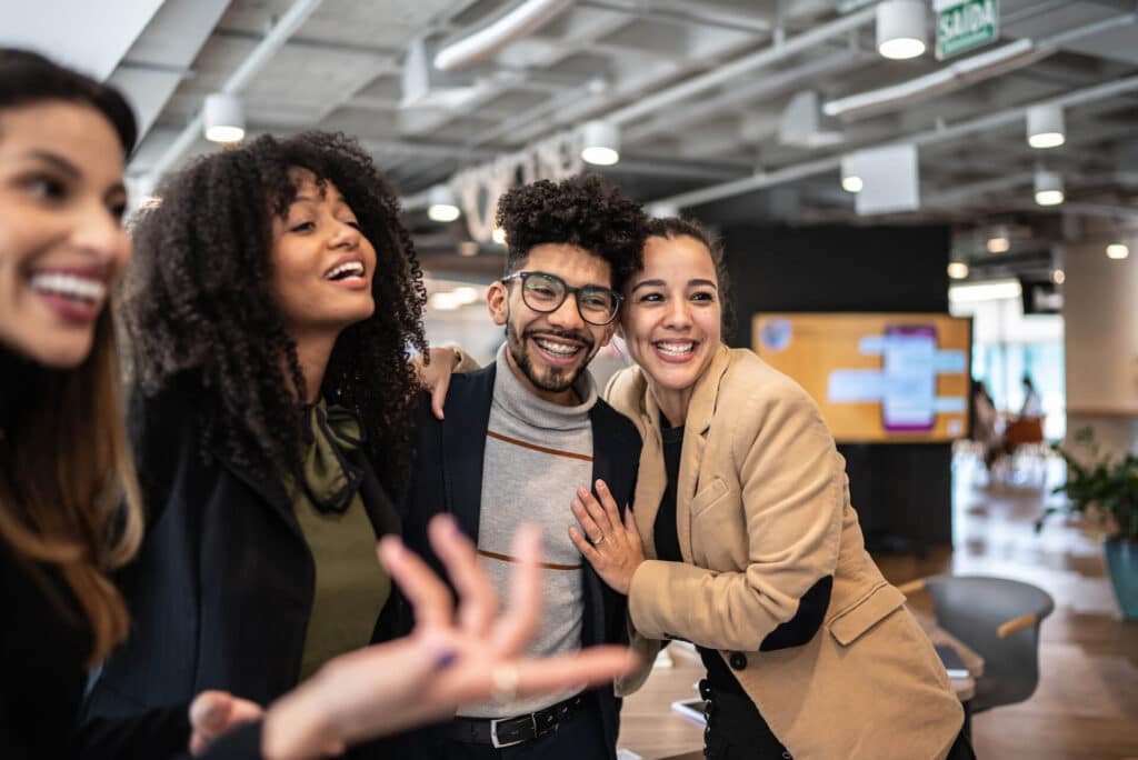 Four people smiling and posing in a modern office space with a blurry, bright interior background.