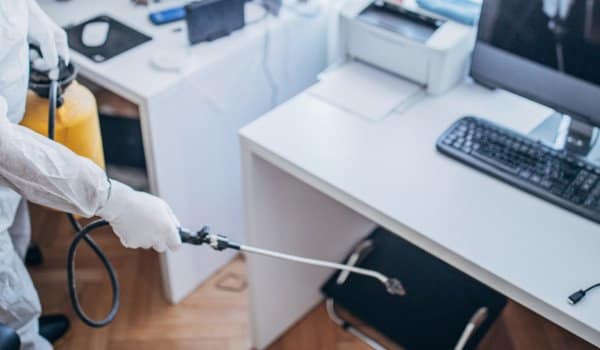 Person in protective gear disinfecting an office desk with a spray.