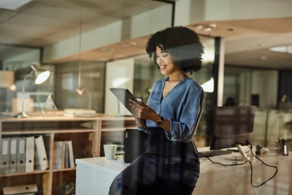 Person sitting on a desk, using a tablet in a modern office setting.