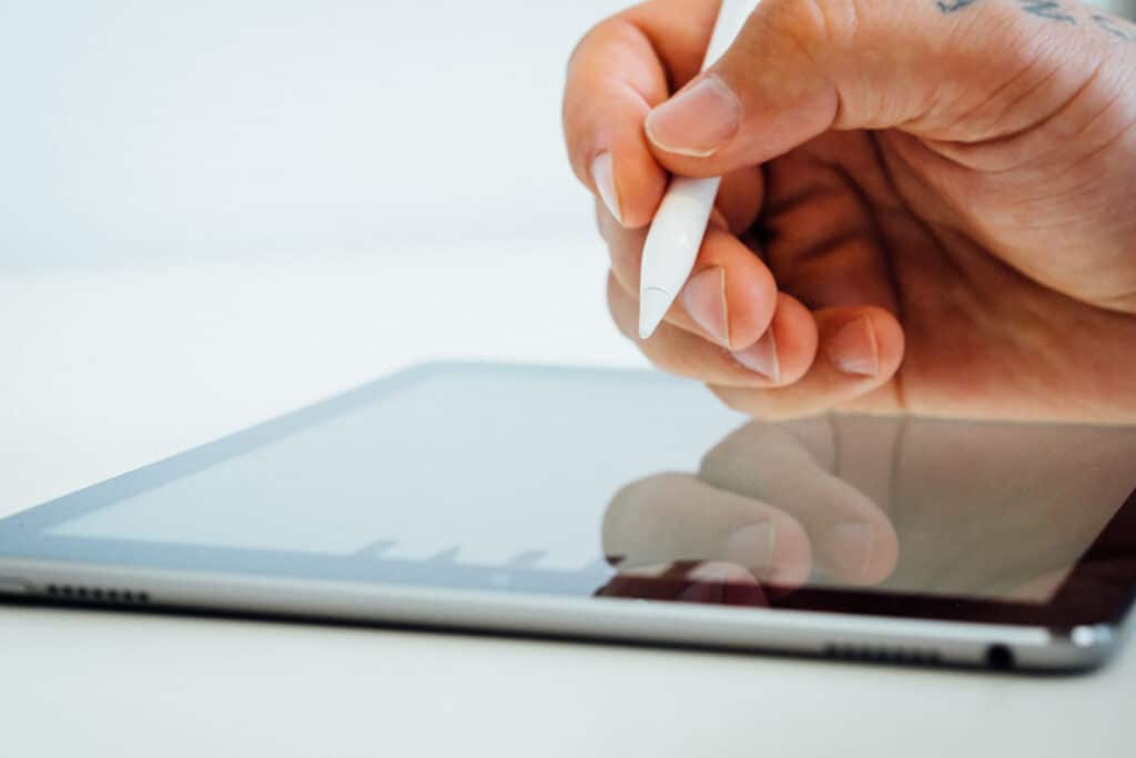 Hand using a stylus on a tablet screen, with a white background.