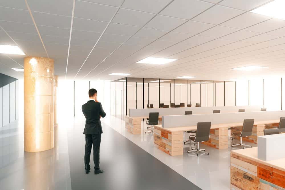 Man in a suit stands in a spacious, empty modern office with rows of desks and chairs.