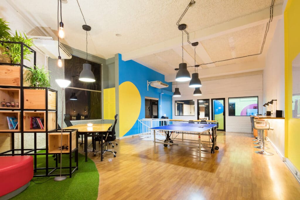 Modern office with ping pong table, bar stools, vibrant walls, and a plant-filled shelving unit.