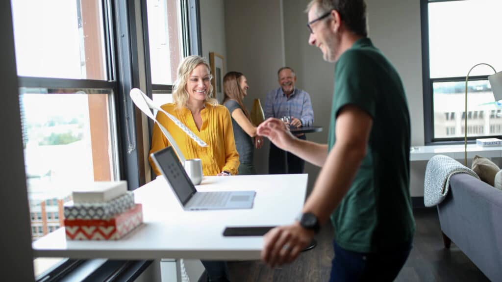 People chatting and smiling around standing desks in a bright office.