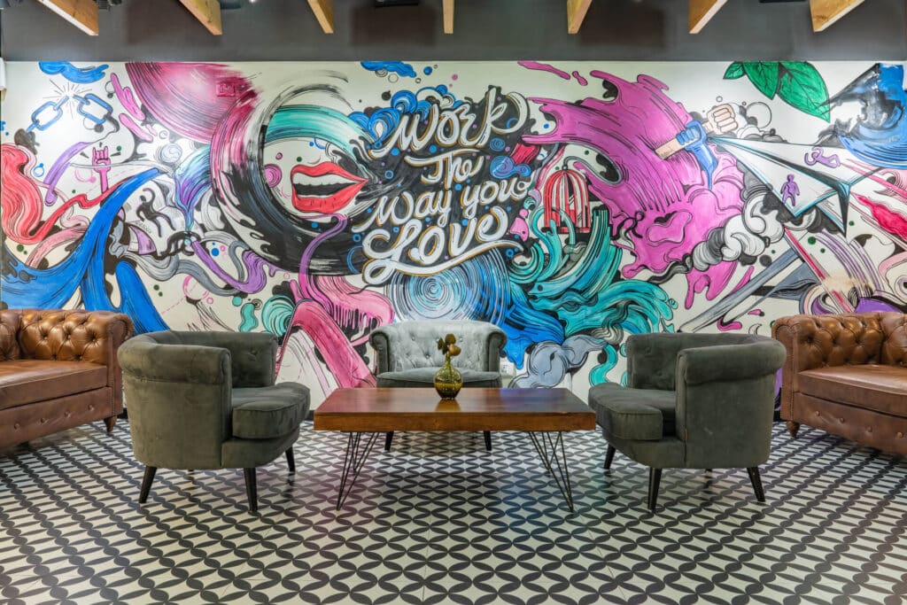 Colorful mural with text "Work the Way You Love" behind vintage sofas and chairs in a stylish lounge.