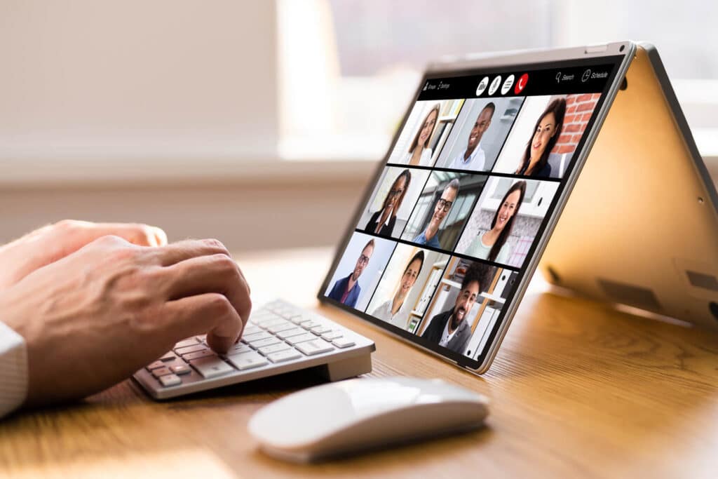 Person typing on a keyboard while participating in a video conference on a tablet showing multiple participants.