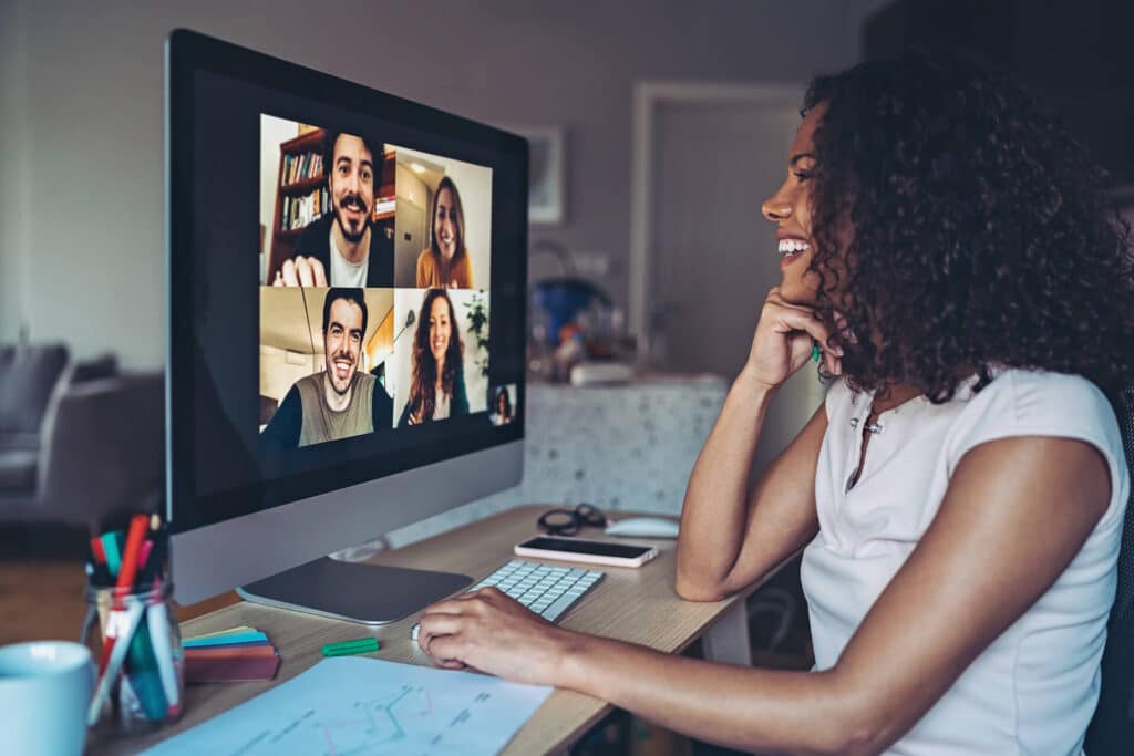 Woman smiling during a video call with four people on a computer screen in a home office setting.