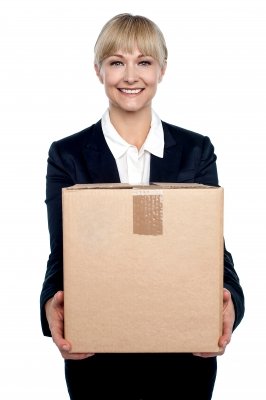 Smiling person in a suit holding a large cardboard box, on a white background.