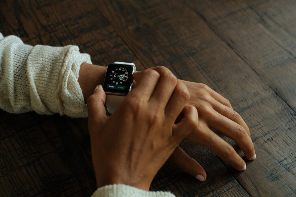 Person wearing a sweater adjusts a smartwatch on their wrist, with a wooden table in the background.