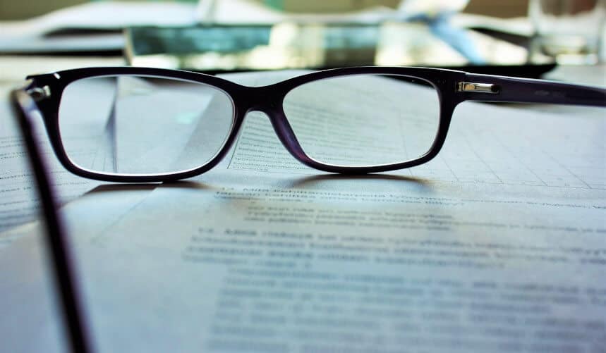 Black eyeglasses resting on documents with blurred text in the background.