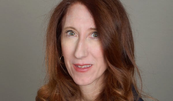 A person with long brown hair is smiling against a neutral background.