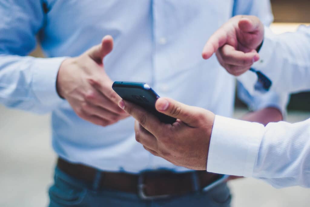 Two people in blue shirts discussing something on a smartphone, with one pointing at the screen.