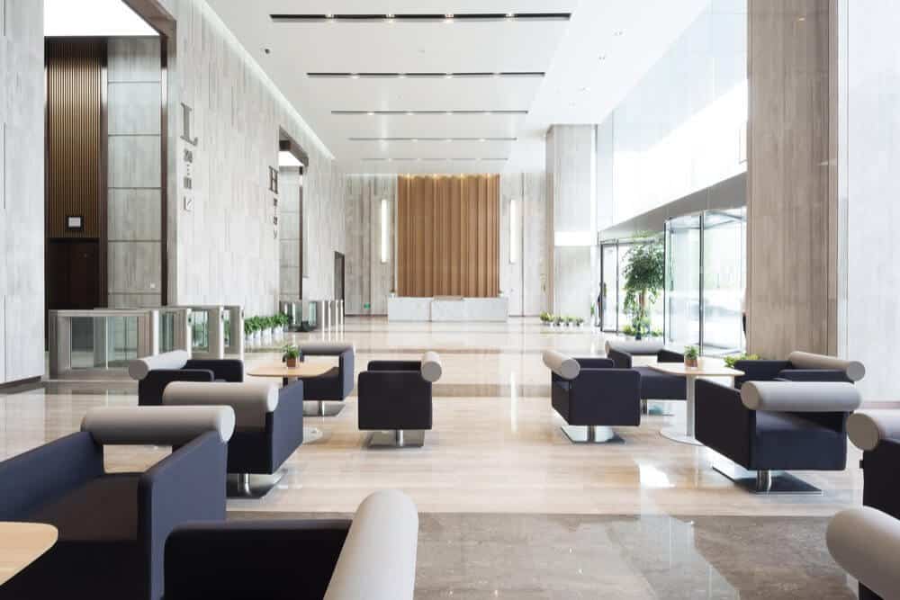 Modern lobby with sleek seating, marble floors, tall windows, and a wooden accent wall behind a white reception desk.
