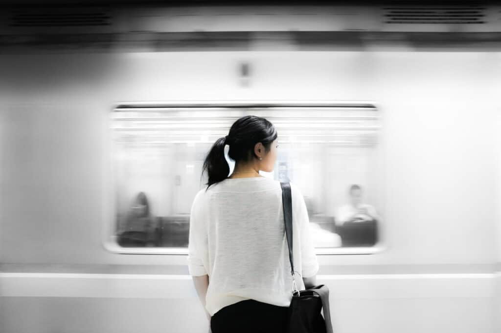 Person with a black ponytail waits as a train rushes past in a subway station.