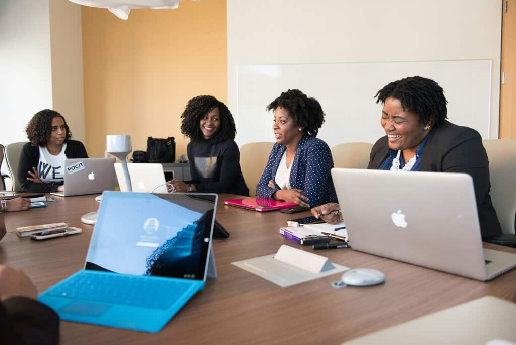Four people sitting at a conference table with laptops, engaged in a meeting and smiling.