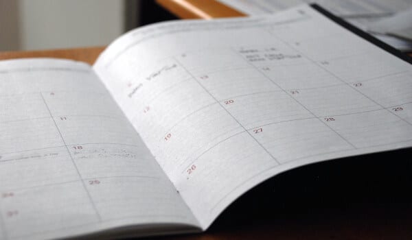 Open planner on a desk showing a monthly calendar with handwritten notes.