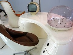 Retro-futuristic workspace with curved chairs, a dome device, and a vintage TV on a sleek white desk.