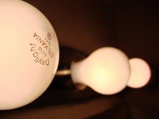 Close-up of three white incandescent light bulbs in a row against a dark background.