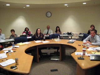 People seated around a large curved conference table, engaging in a meeting with papers and drinks on the table.