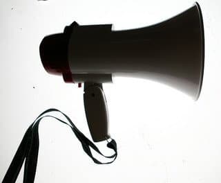 Side view of a white megaphone with a black handle and strap on a light background.