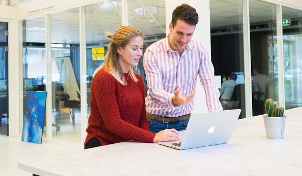 Two people at a desk looking at a laptop screen in a modern office setting.