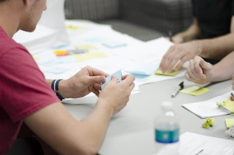 People collaborating at a table with papers, sticky notes, and a water bottle.