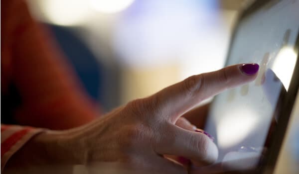 A hand with purple nail polish taps on a tablet screen.