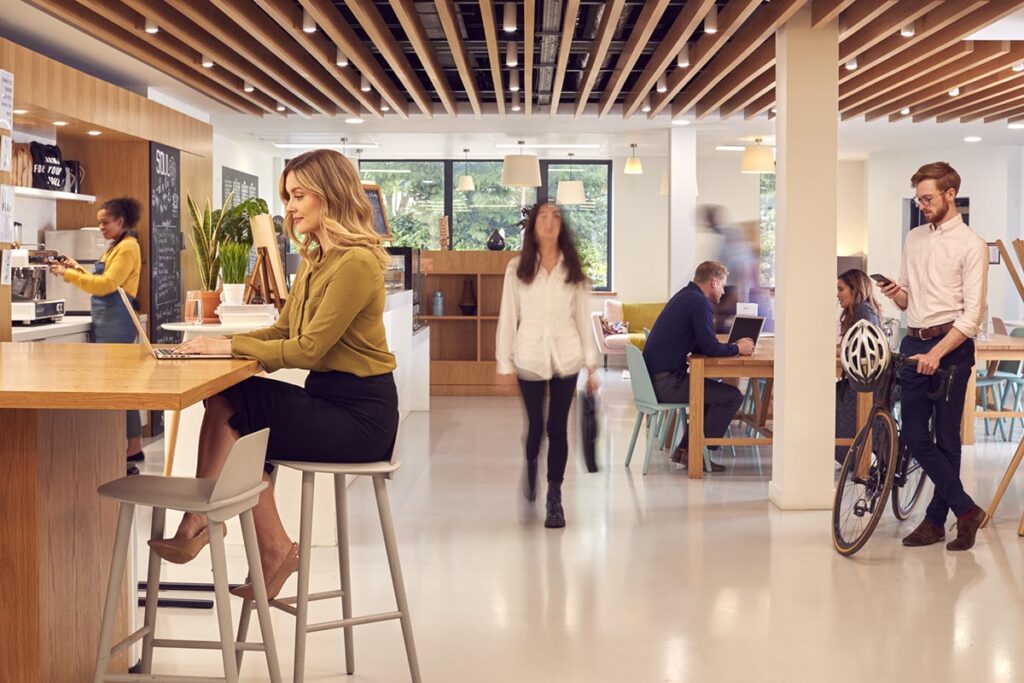 Modern office with people working, chatting, and walking; includes a cyclist holding a bike and a woman using a laptop.