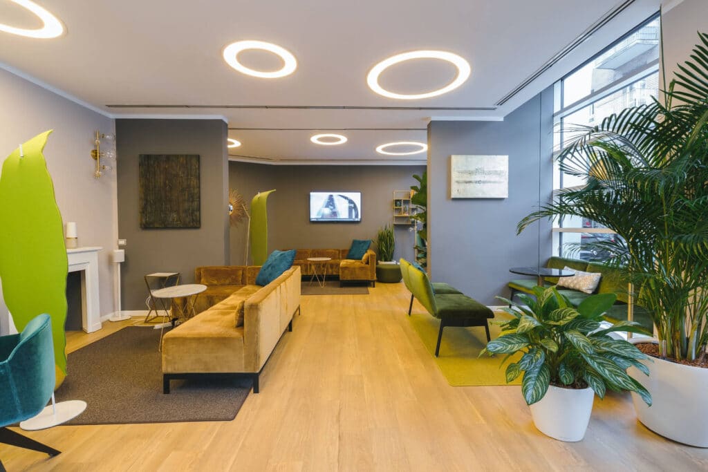 Modern lounge with circular ceiling lights, plants, velvet chairs, and a wall-mounted TV.