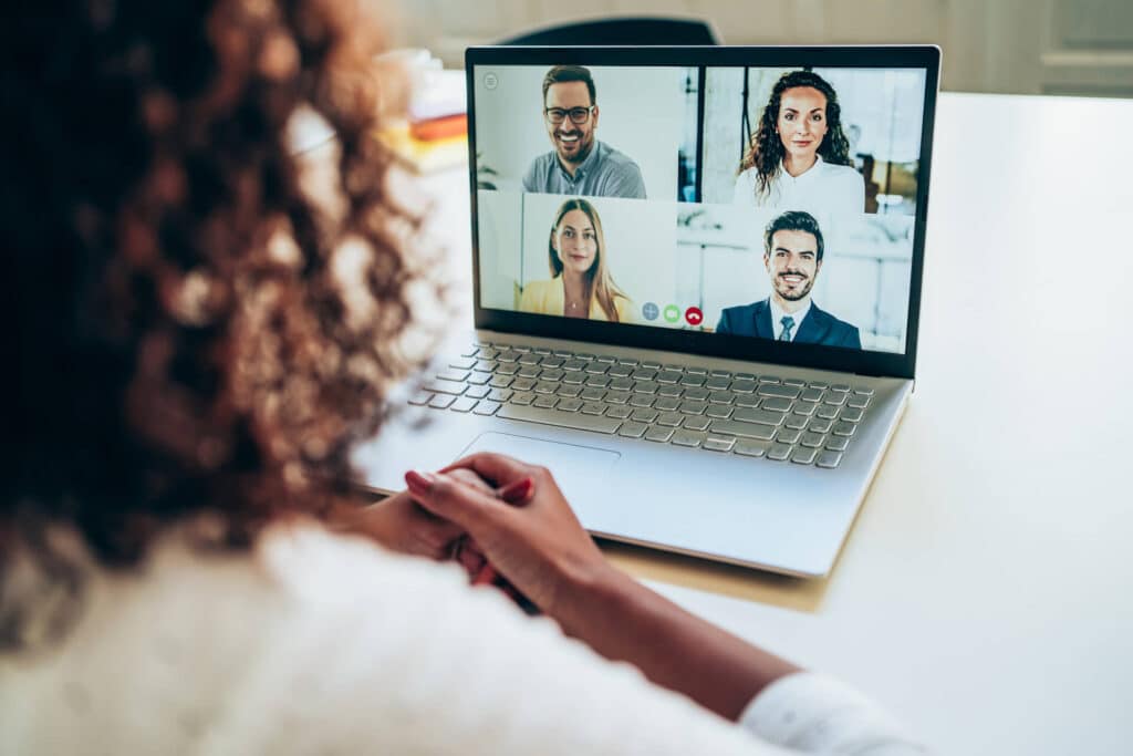 Person having a video call on a laptop with four people, sitting at a white desk.