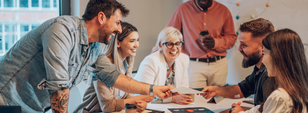 Group of colleagues smiling and sharing documents during a meeting in a bright office.