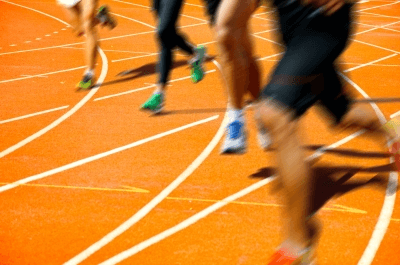 Blurry image of athletes running on an orange track, focusing on their legs and shoes.
