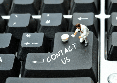 A miniature figure painting "Contact Us" on a computer keyboard's Enter key.