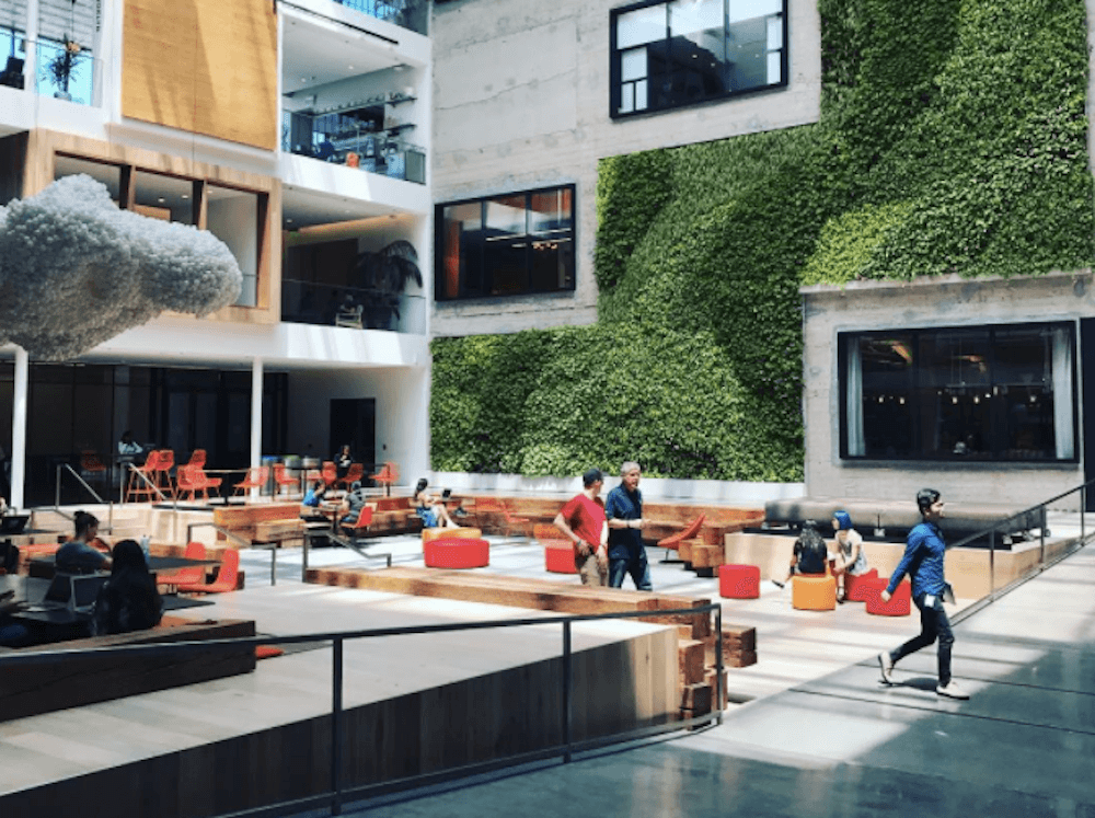 Modern indoor atrium with green wall, seating areas, and people walking and sitting.