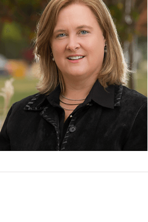 Person with shoulder-length hair wearing a black jacket and shirt, smiling outdoors.