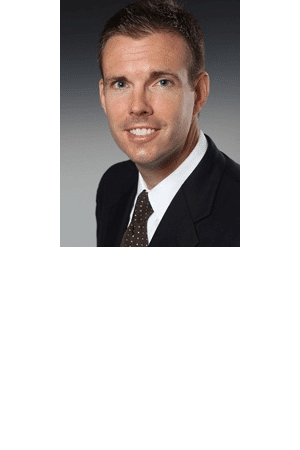 Man in a suit with a brown tie, smiling, against a gray background.